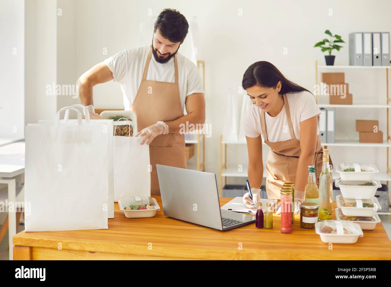 Positivi i giovani addetti ai servizi di consegna degli alimenti che lavorano con gli ordini online imballaggio di pasti sani in scatole Foto Stock