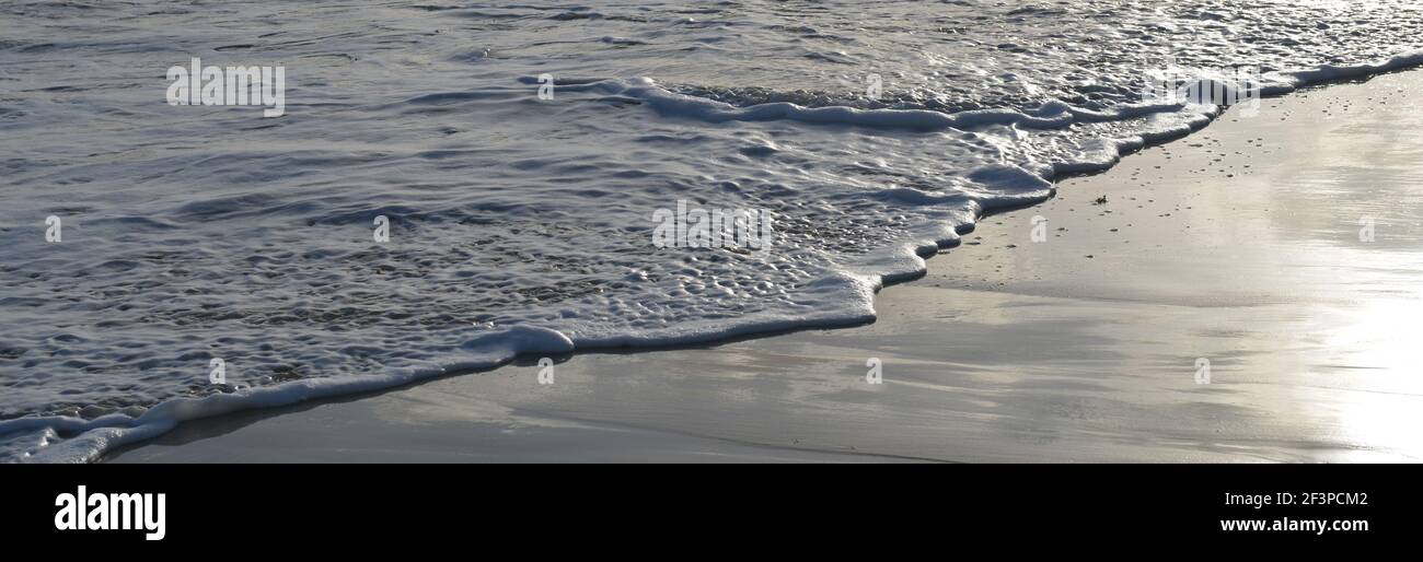 Striscione di schiuma bianca di un'onda morbida sul spiaggia la sera Foto Stock