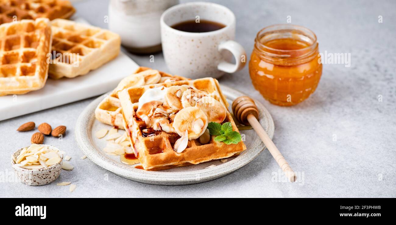 Cialde belghe dolci con salsa di banana e caramello su un piatto. La colazione comprende waffle e caffè Foto Stock