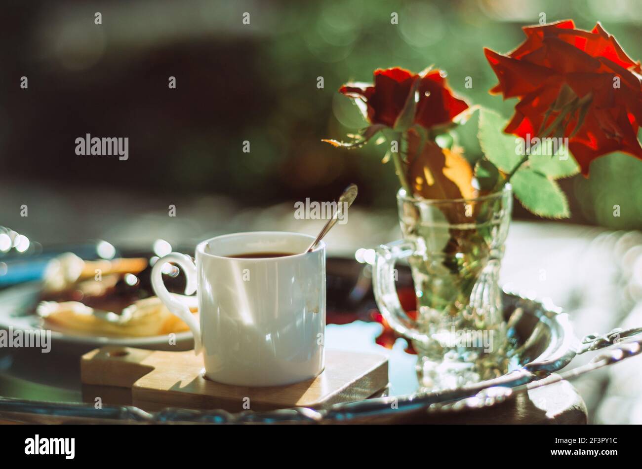 Brunch all'aperto con primo piano di una tazza di caffè espresso su un piatto d'argento vintage e rose, bokeh sfondo Foto Stock