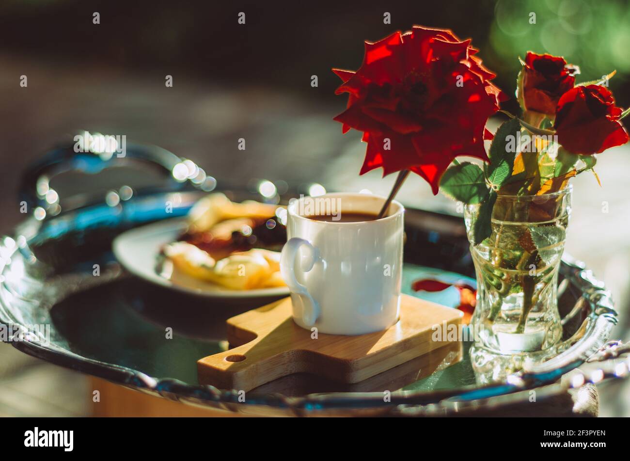 Brunch all'aperto con primo piano di una tazza di caffè espresso su un piatto d'argento vintage e rose, sfondo verde bokeh Foto Stock