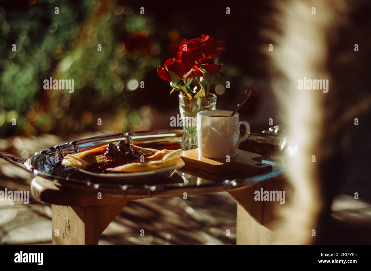 Ancora vita shot di vassoio della colazione argento piatto con tazza di caffè, rose e frittelle bagnati in luce dorata, e gatto coda foto bombardamento Foto Stock