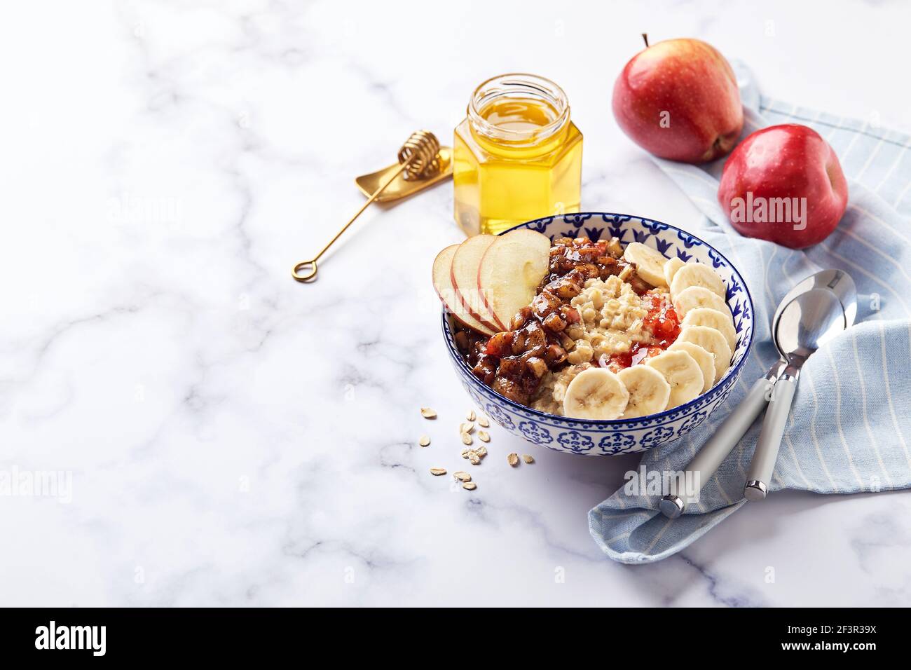 Porridge d'avena con mele caramellate con cannella, banana, fragole grattugiate e miele su sfondo di marmo chiaro Foto Stock