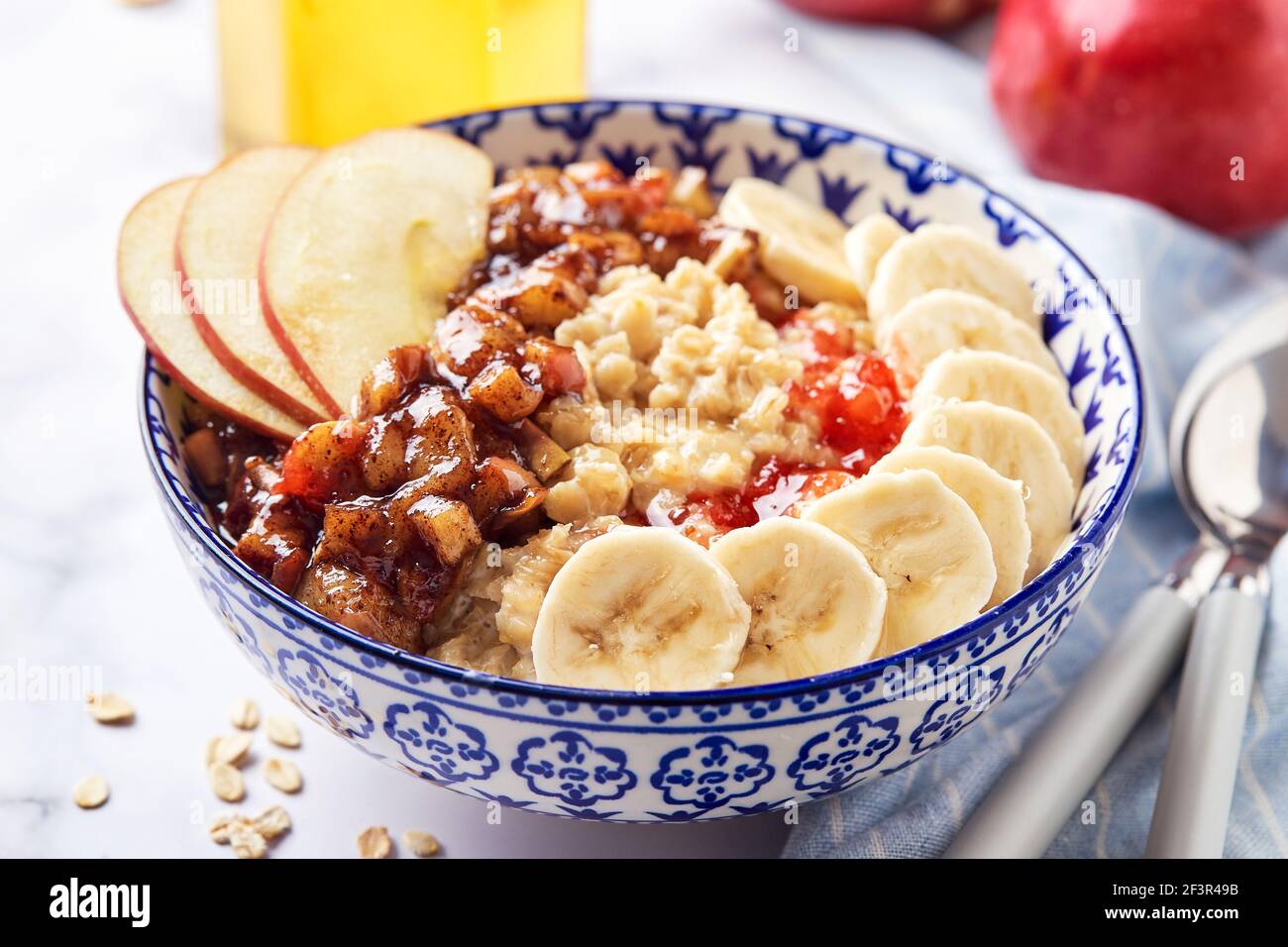 Porridge d'avena con mele caramellate con cannella, banana, fragole grattugiate e miele su sfondo di marmo chiaro, primo piano Foto Stock
