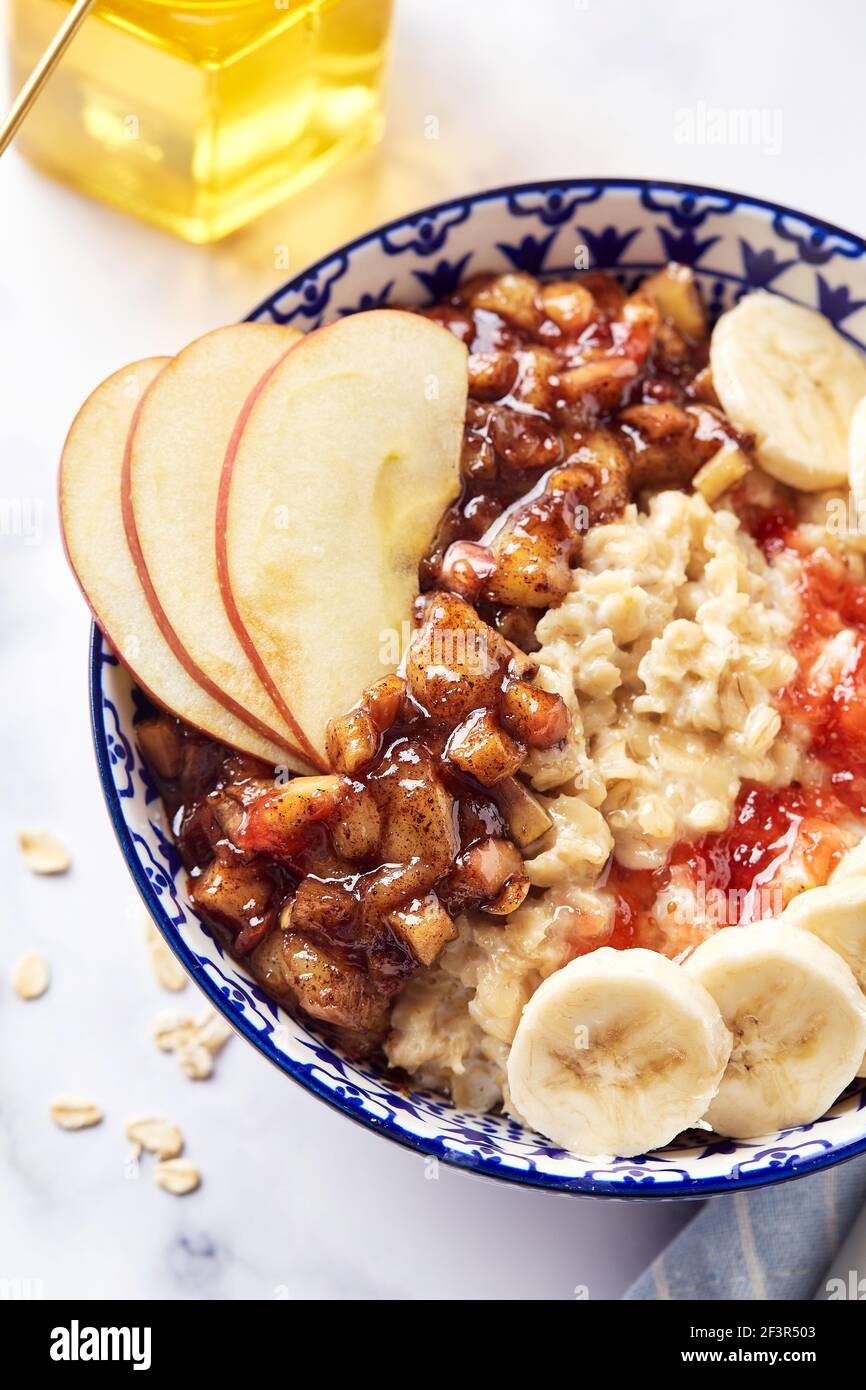 Porridge d'avena con mele caramellate con cannella, banana, fragole grattugiate e miele su sfondo di marmo chiaro, primo piano Foto Stock