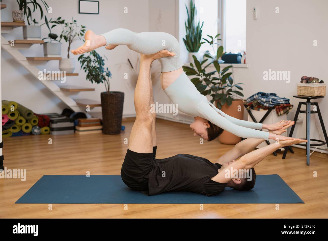 Giovane coppia che pratica acro yoga insieme a casa in un interno moderno. Hobby, togetherness, stile di vita sano Foto Stock