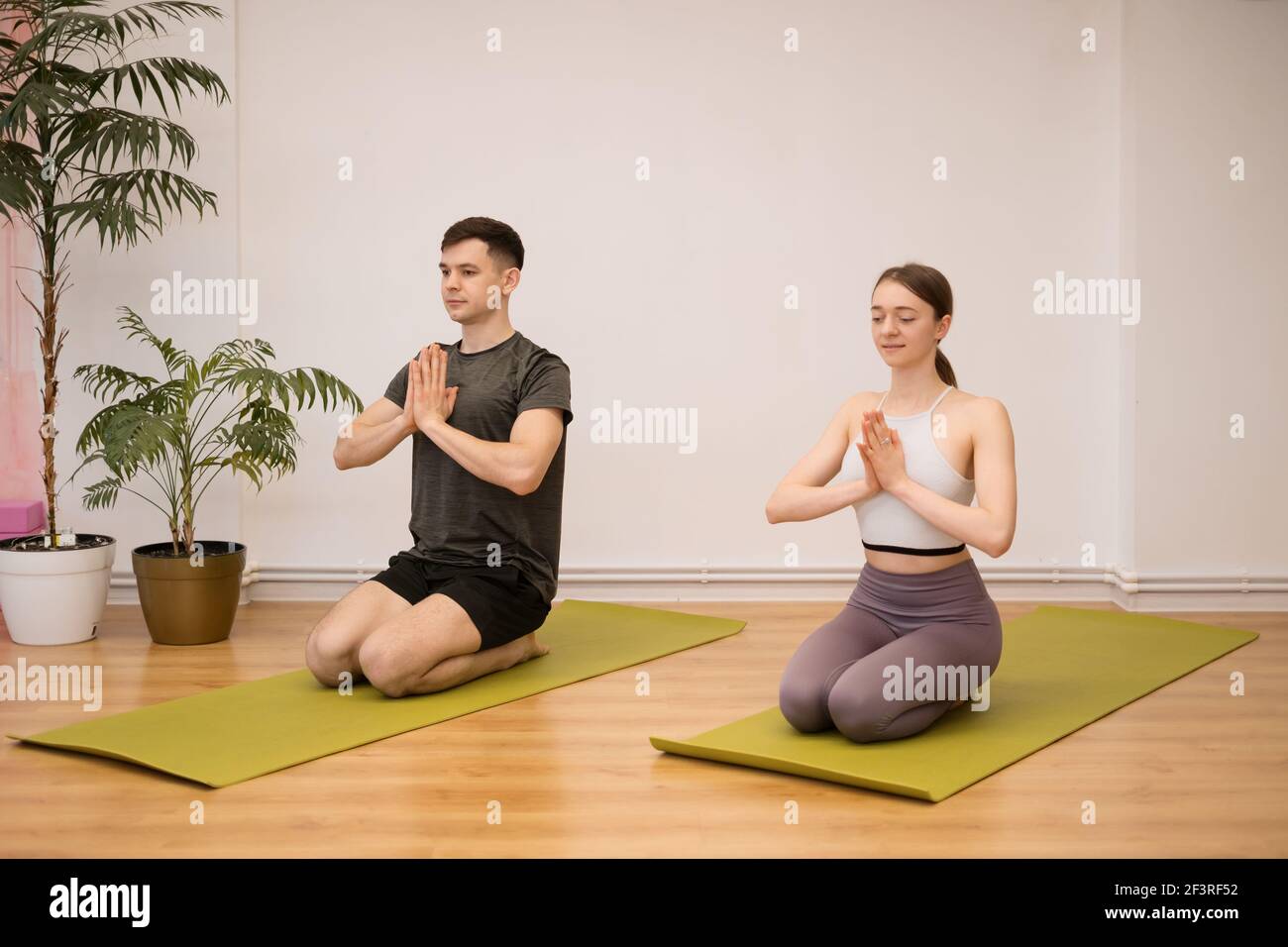 Giovane coppia che pratica yoga insieme a casa in un interno moderno. Hobby, togetherness, stile di vita sano Foto Stock