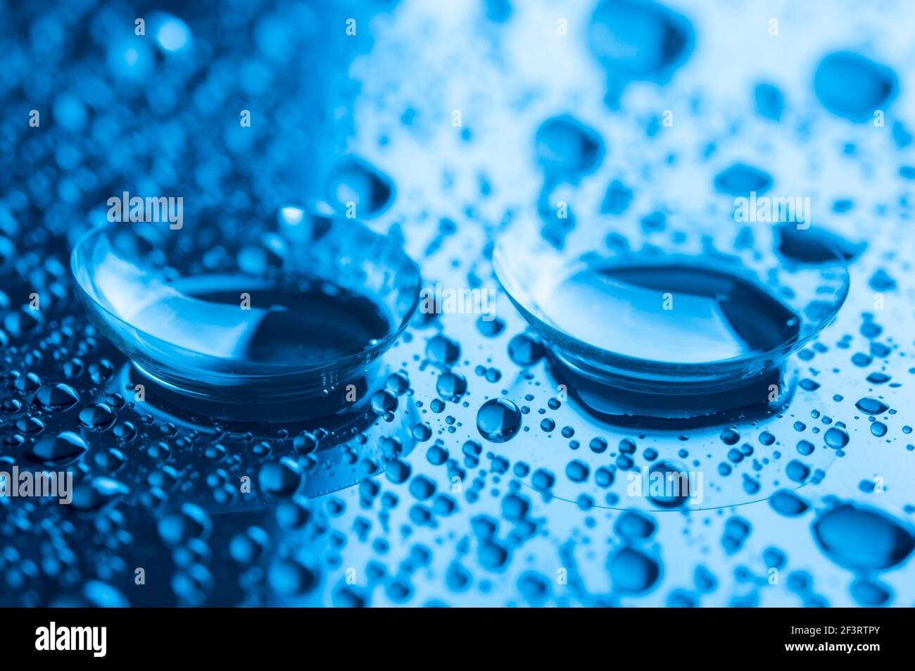 Primo piano di due lenti a contatto con gocce su sfondo scuro. Immagine con tonalità blu. Foto Stock