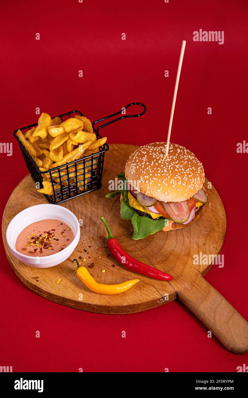 Un hamburger grande, patatine fritte, salsa fritta e due peperoncini serviti su una tavola di legno Foto Stock