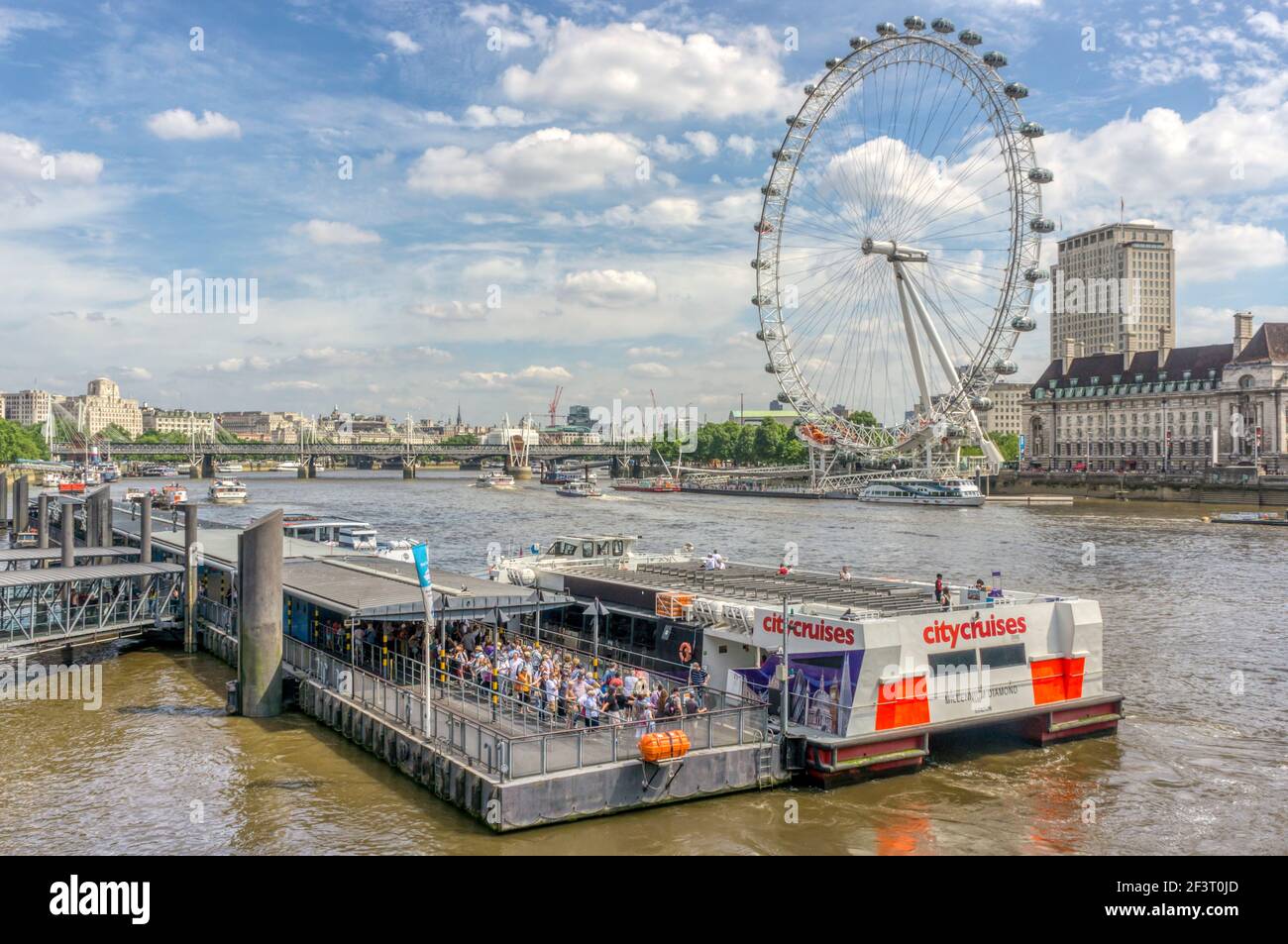 Molo di Westminster con persone a bordo di una gita in barca sul fiume City Cruises e il London Eye visto attraverso il Tamigi in una soleggiata giornata estiva. Foto Stock