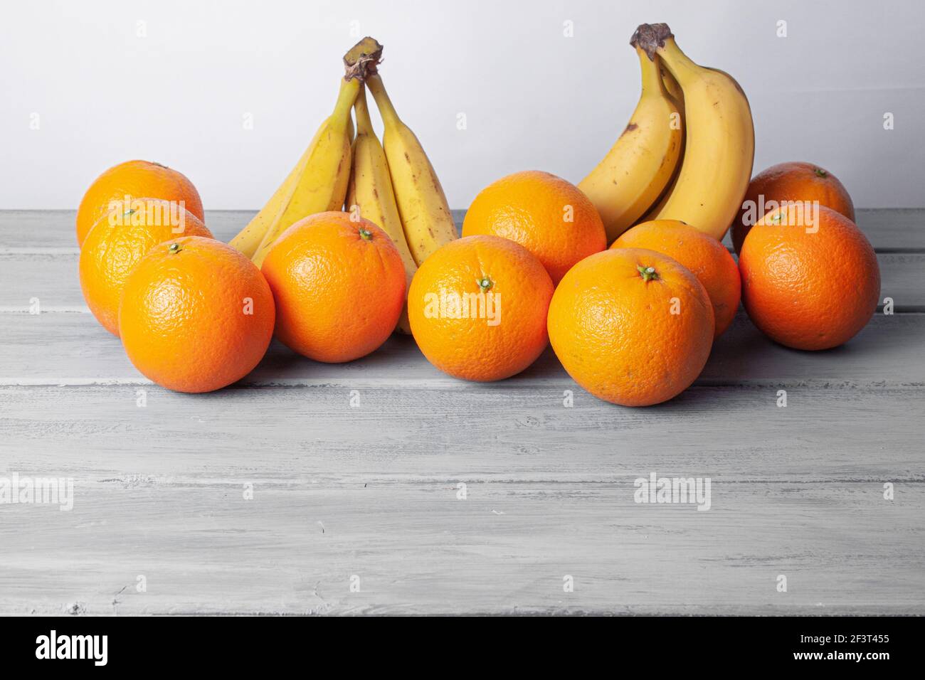 Vista delle arance e delle banane allineate su un grigio tabella su sfondo bianco Foto Stock