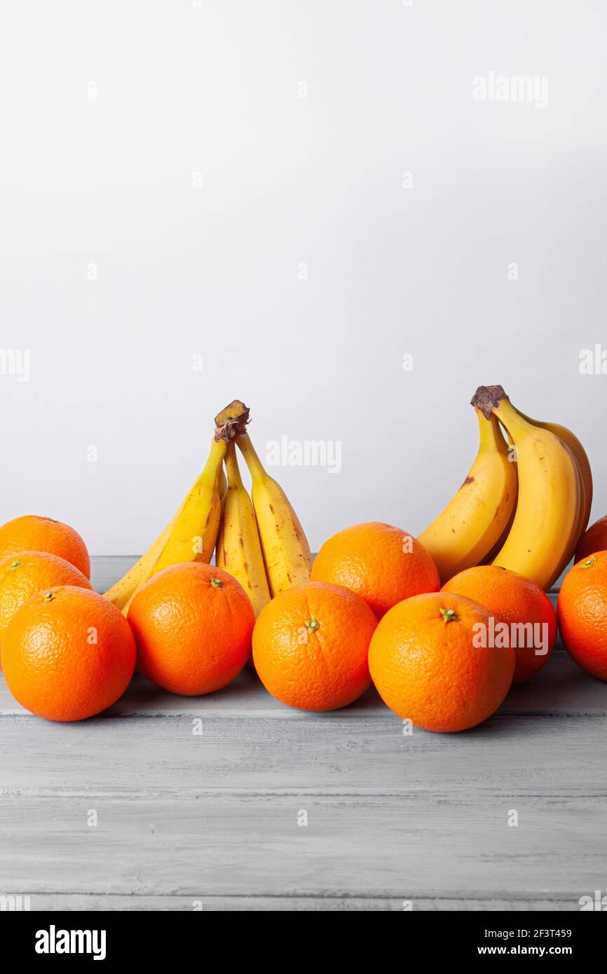 Vista delle arance e delle banane allineate su un grigio tabella su sfondo bianco Foto Stock