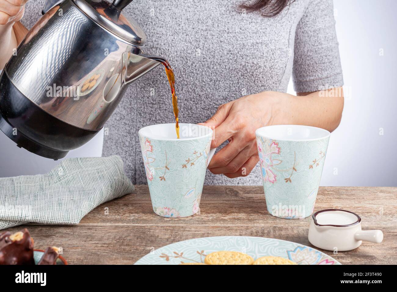 un concetto di tempo del tè o del caffè con biscotti sandwich, barrette di tazza di ceramica estetica al cioccolato e piatti, nonché una mini caraffa crematrice su legnoso Foto Stock
