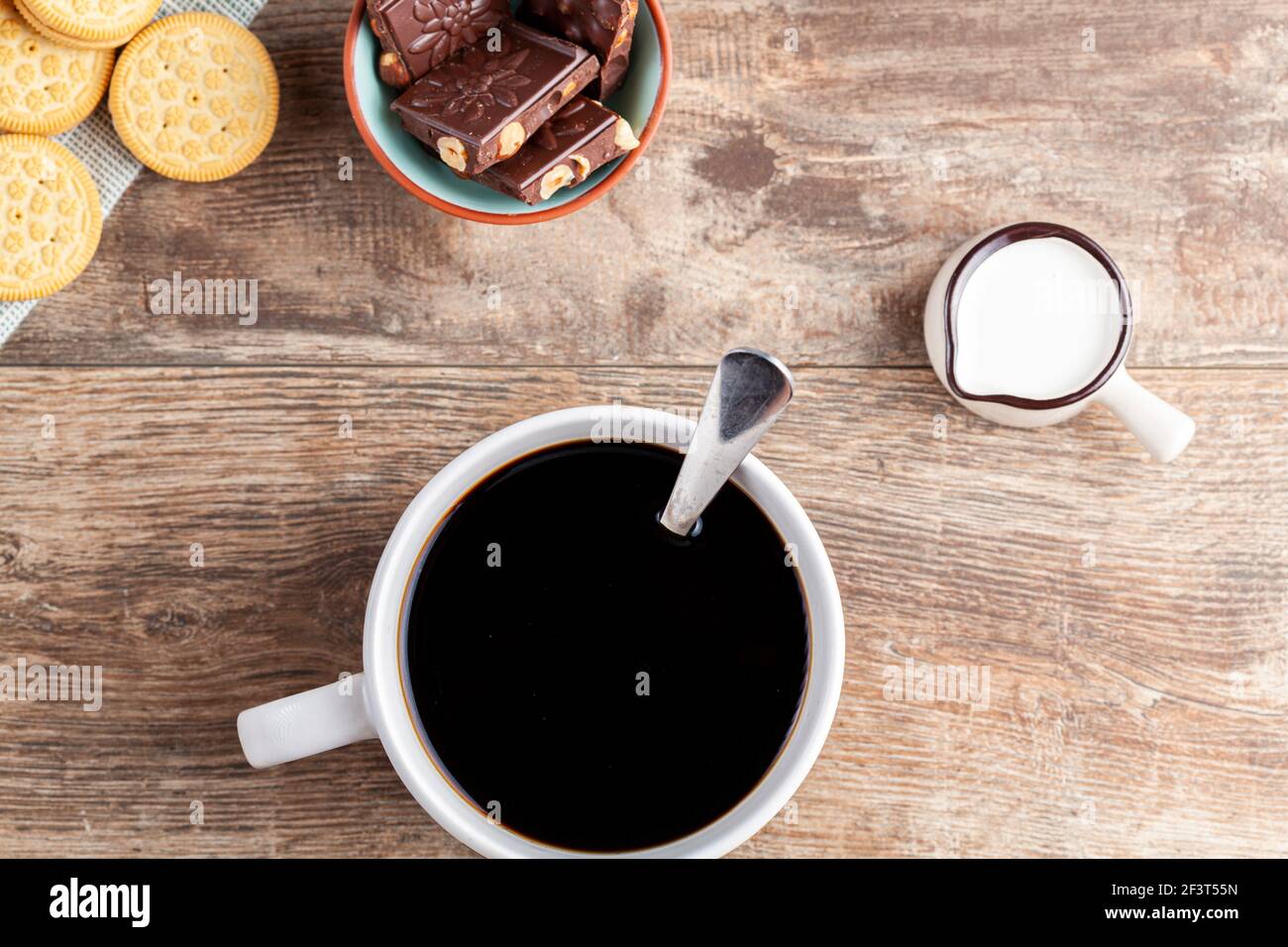un concetto di tempo del tè o del caffè con biscotti sandwich, barrette di tazza di ceramica estetica al cioccolato e piatti, nonché una mini caraffa crematrice su legnoso Foto Stock