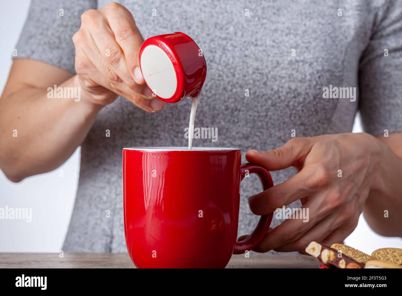 un concetto di tempo del tè o del caffè con biscotti sandwich, barrette di tazza di ceramica estetica al cioccolato e piatti, nonché una mini caraffa crematrice su legnoso Foto Stock