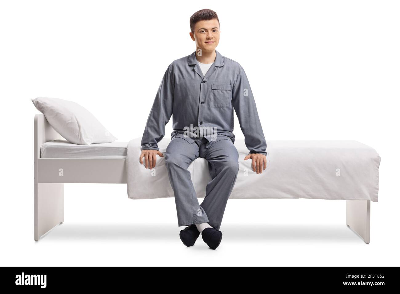 Giovane in pigiama seduto su un letto singolo isolato su sfondo bianco Foto Stock