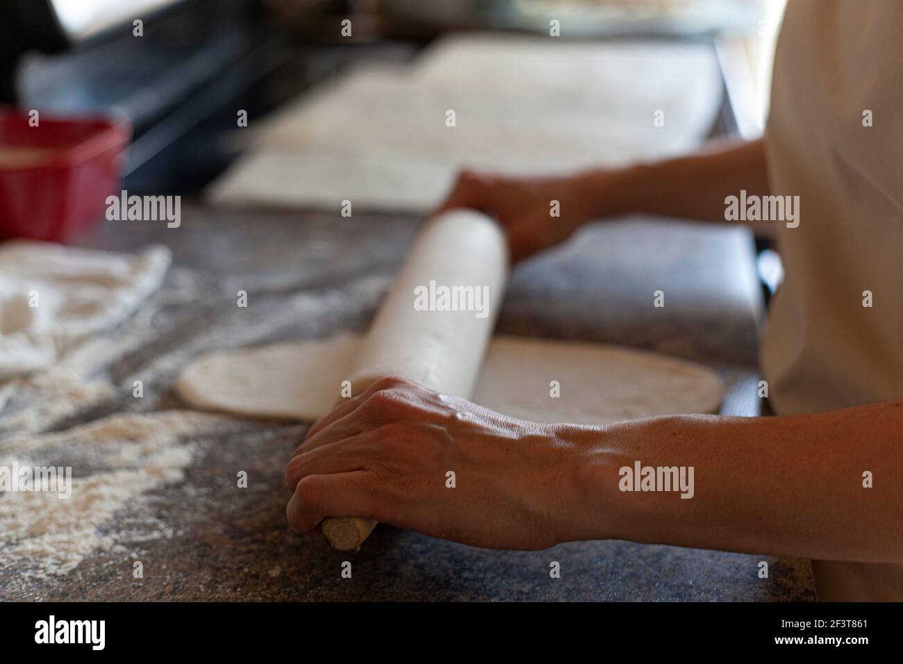 Una donna caucasica sta usando un perno di rotolamento americano per rotolare sopra gli impasti del pane per appiattirli e modellarli. Autentico sfondo cucina fatta in casa pane ma Foto Stock