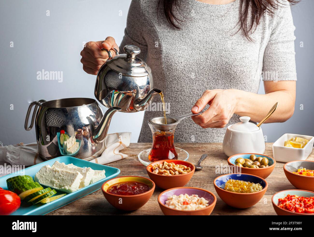 Sana colazione turca, con pomodoro a fette, cetriolo e formaggio feta bianco, piccole ciotole di marmellata di fragole, olive, miele, pasta di pepe. Il tè è versato Foto Stock