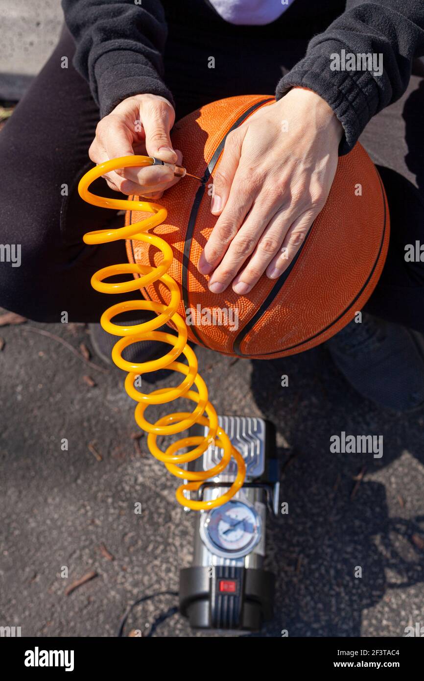 Primo piano immagine che mostra una donna caucasica che tiene un basket e inserendo la punta dell'ago all'estremità del tubo fissato al dispositivo di gonfiaggio pneumatici per auto da 12 v a p. Foto Stock