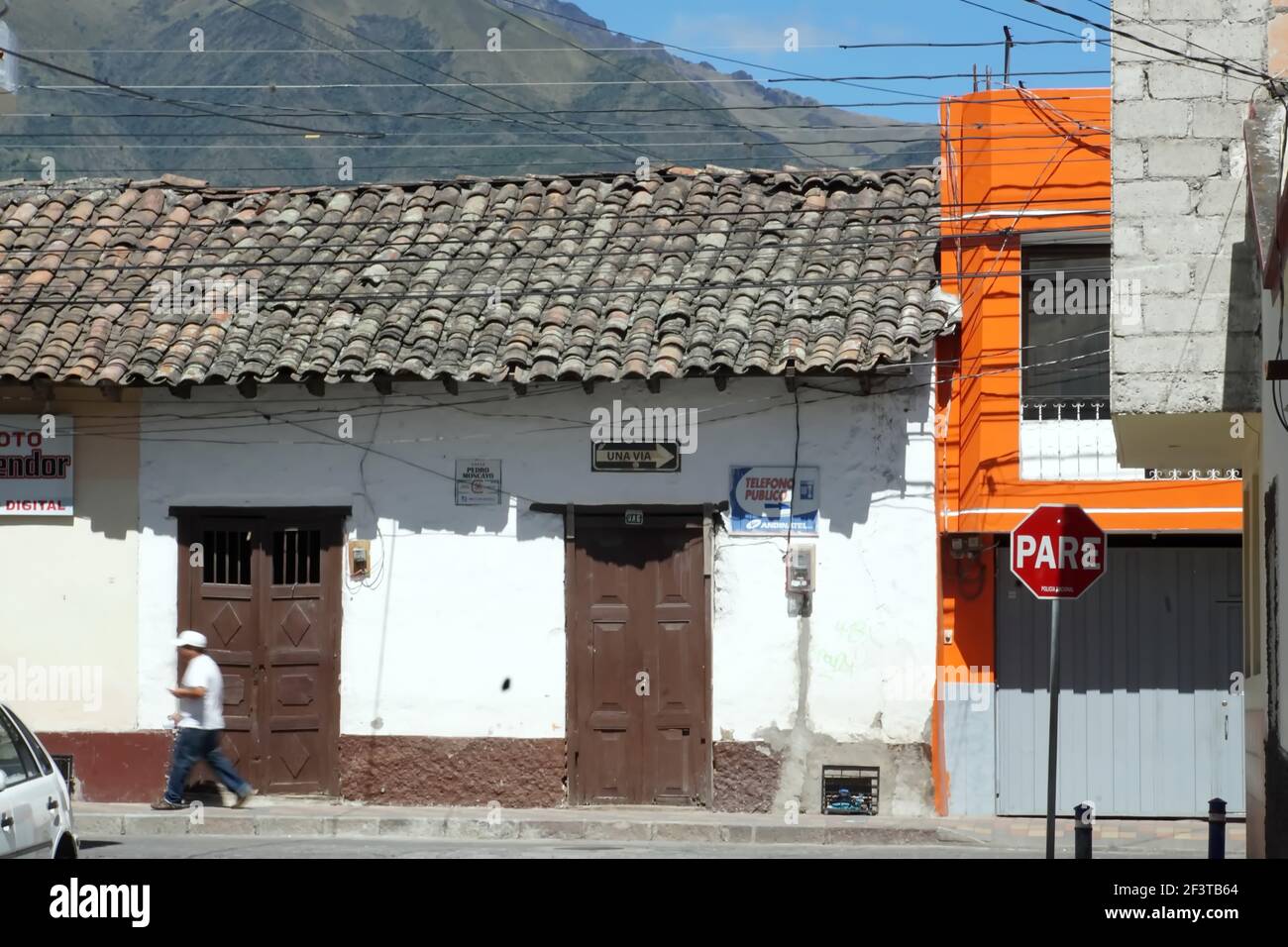 Uomo sul marciapiede, a piedi davanti a una porta marrone in un vecchio edificio con un tetto in piastrelle a Cotacachi, Ecuador Foto Stock