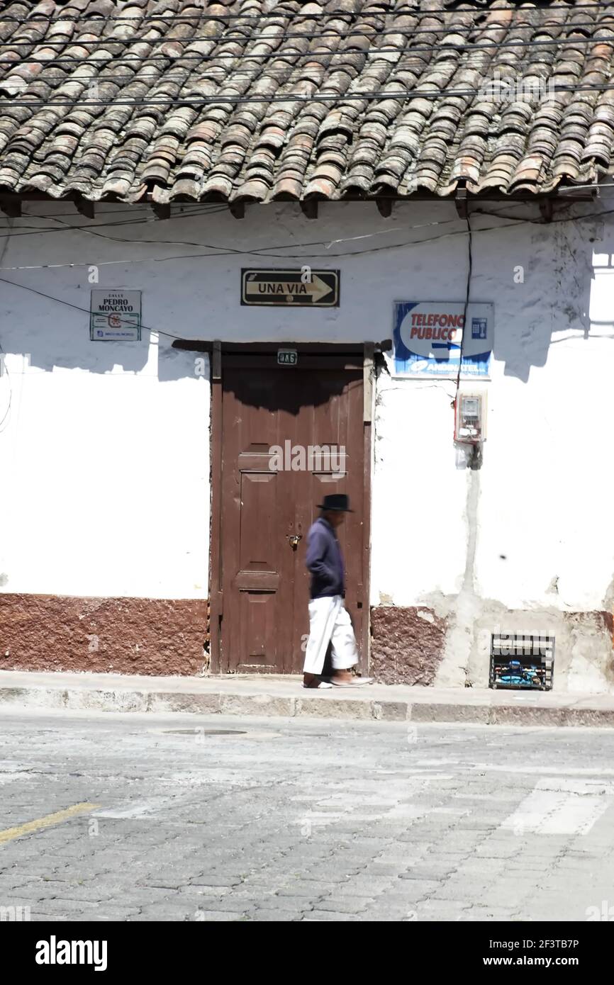 Uomo sul marciapiede, a piedi davanti a una porta marrone in un vecchio edificio con un tetto in piastrelle a Cotacachi, Ecuador Foto Stock