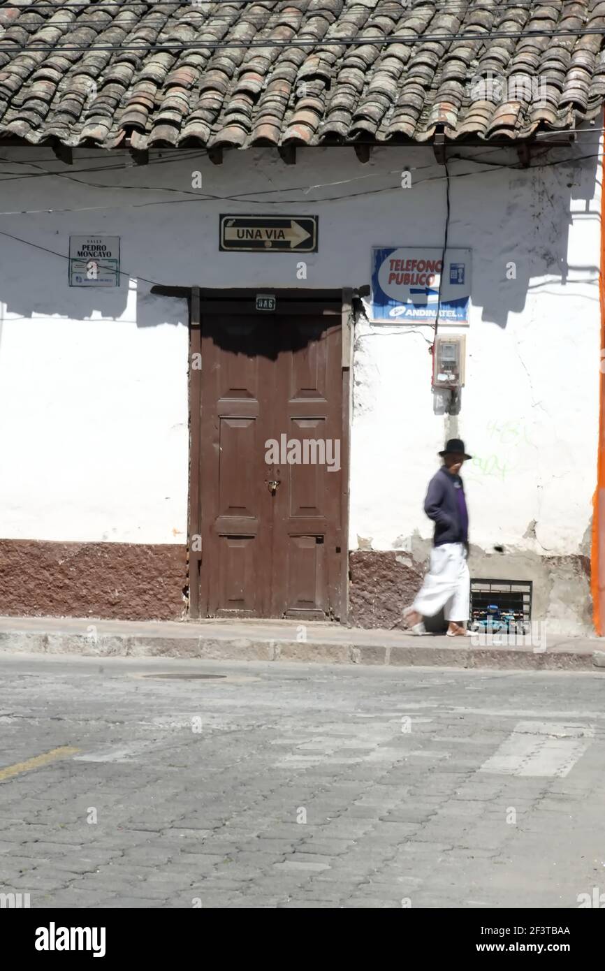 Uomo sul marciapiede, a piedi davanti a una porta marrone in un vecchio edificio con un tetto in piastrelle a Cotacachi, Ecuador Foto Stock