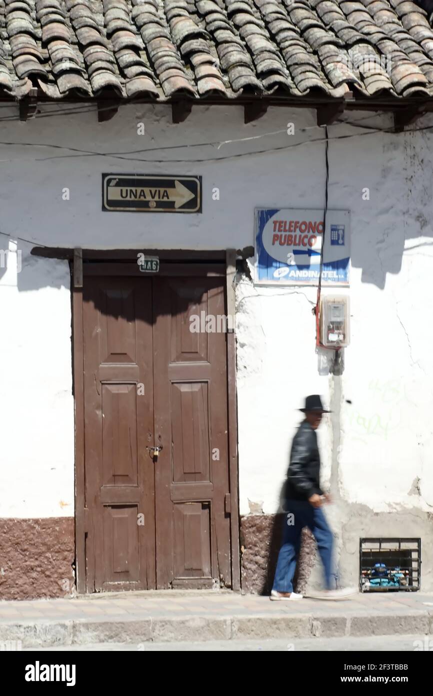 Uomo sul marciapiede, a piedi davanti a una porta marrone in un vecchio edificio con un tetto in piastrelle a Cotacachi, Ecuador Foto Stock