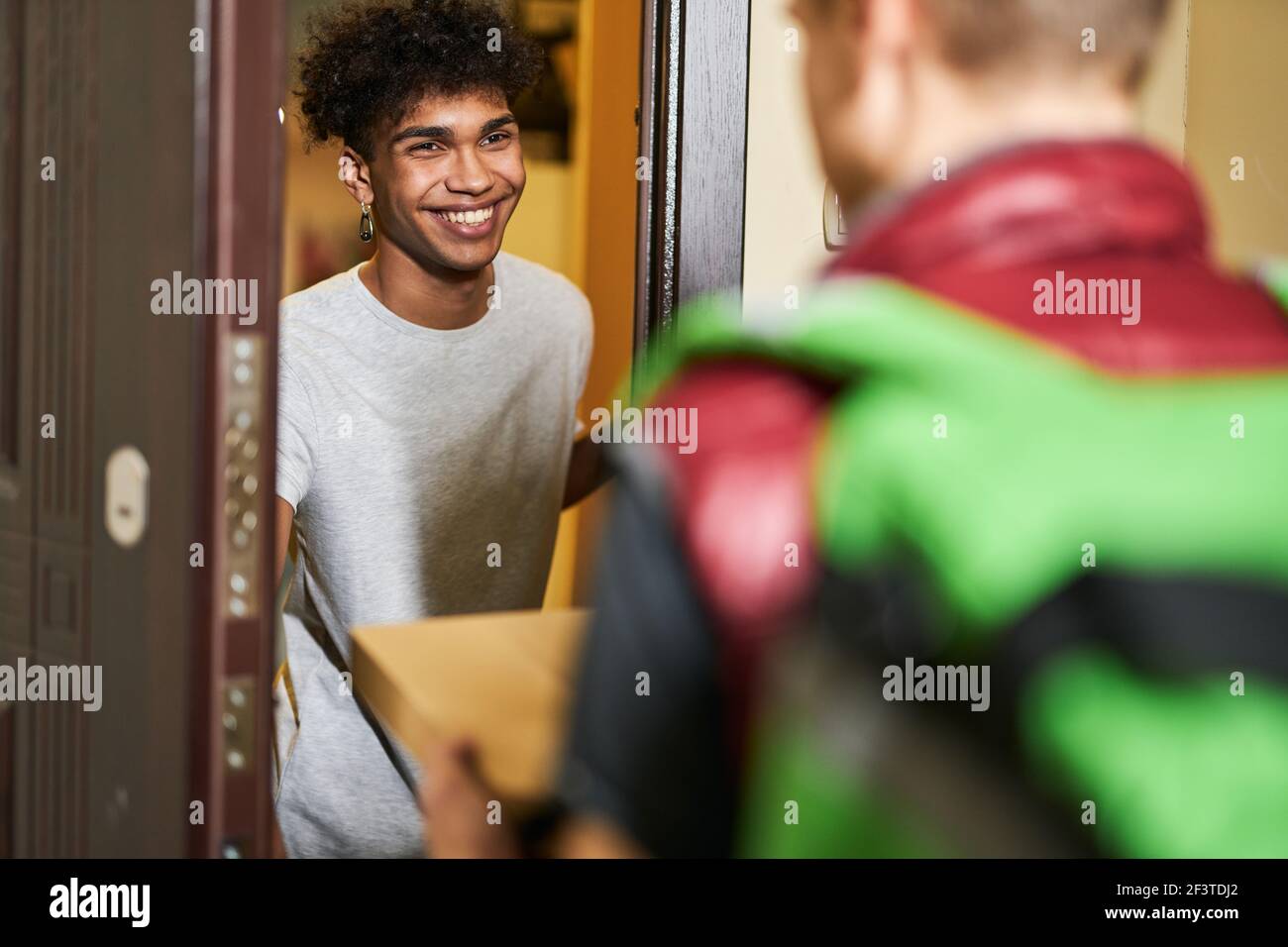 Il suo tempo di pizza. Ragazzo giovane che cerca felice mentre incontra il corriere con la scatola della pizza, passare il tempo a casa da solo Foto Stock