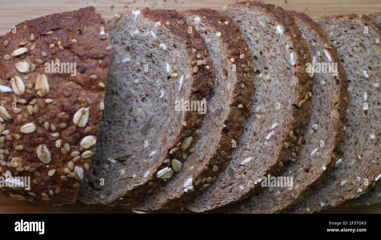 Affettare il pane di grano intero su un tavolo di legno Foto Stock
