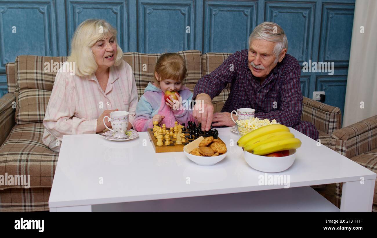 Nonni anziani e nipote che trascorrono il tempo a casa insieme, seduti, giocando a scacchi Foto Stock