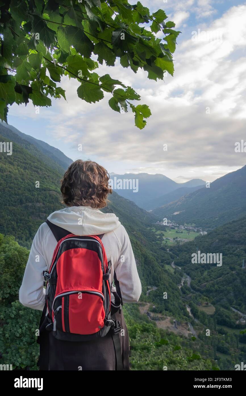 Giovane donna sulla schiena contempla da un punto di vista, un paesaggio montano nella Valle di Aran, con il villaggio di Bosost sullo sfondo, copia spa Foto Stock