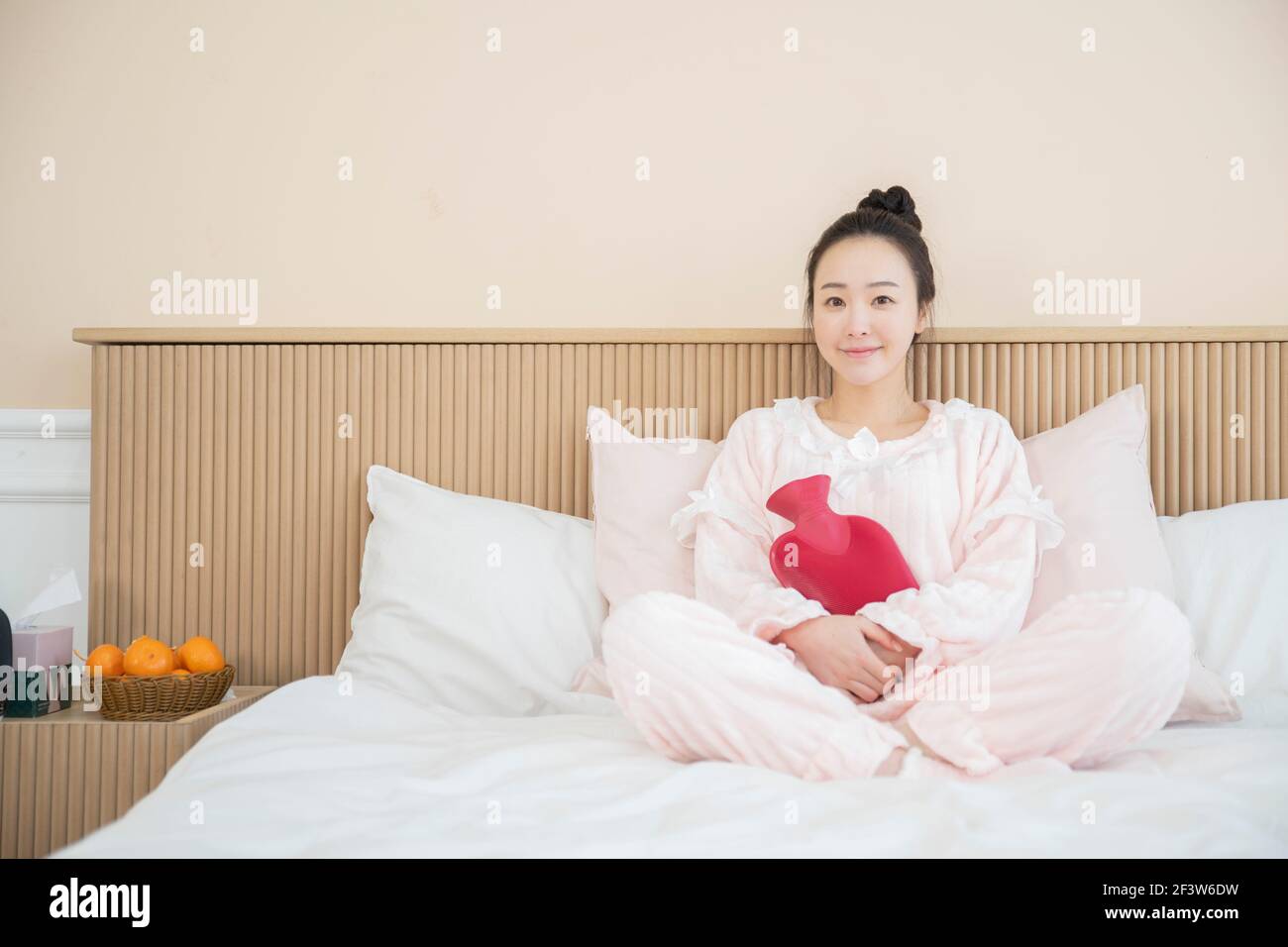 Donna asiatica con pigiami rosa a letto sacchetto d'acqua tiepida in gomma Foto Stock