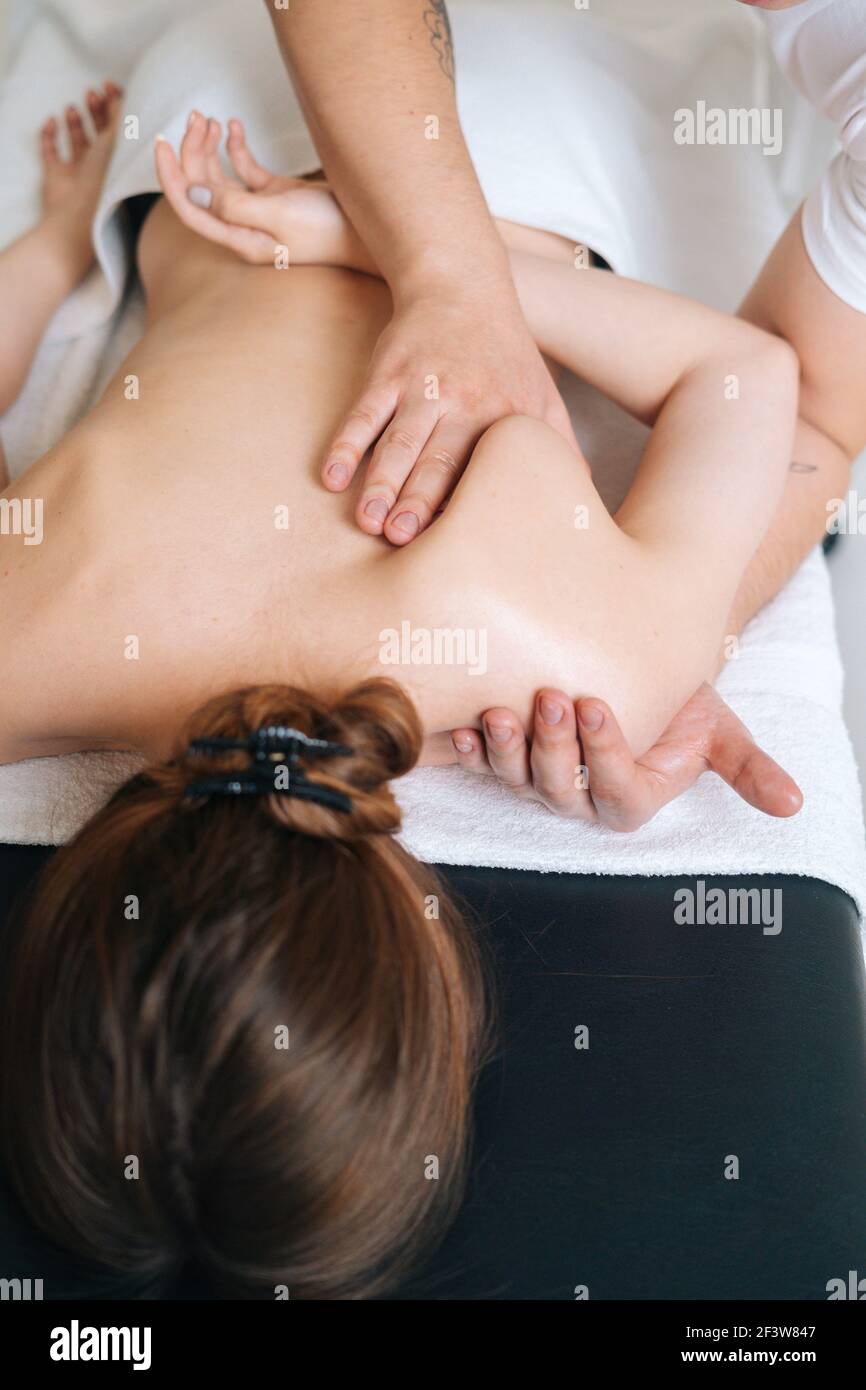 Vista dall'alto del massaggiatore maschile che massaggia la parte posteriore della giovane donna sdraiata sul tavolo da massaggio. Foto Stock