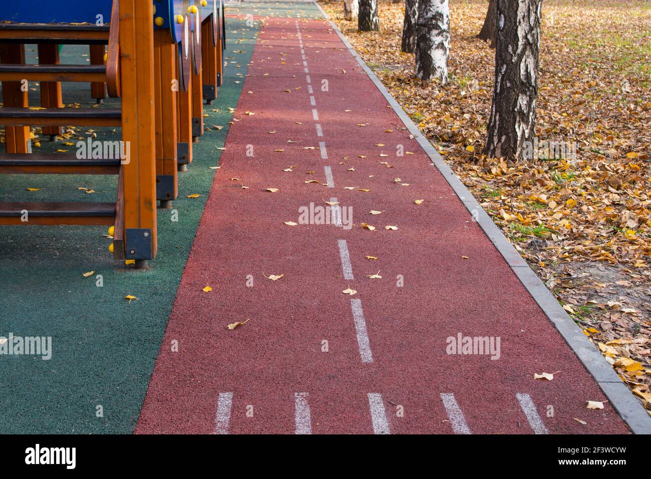 Tapis roulant è fatto di rivestimento in gomma antiscivolo di colore borgogna, con linea punteggiata bianca, lungo il parco giochi sulla sinistra e un marciapiede con un certo numero di Foto Stock