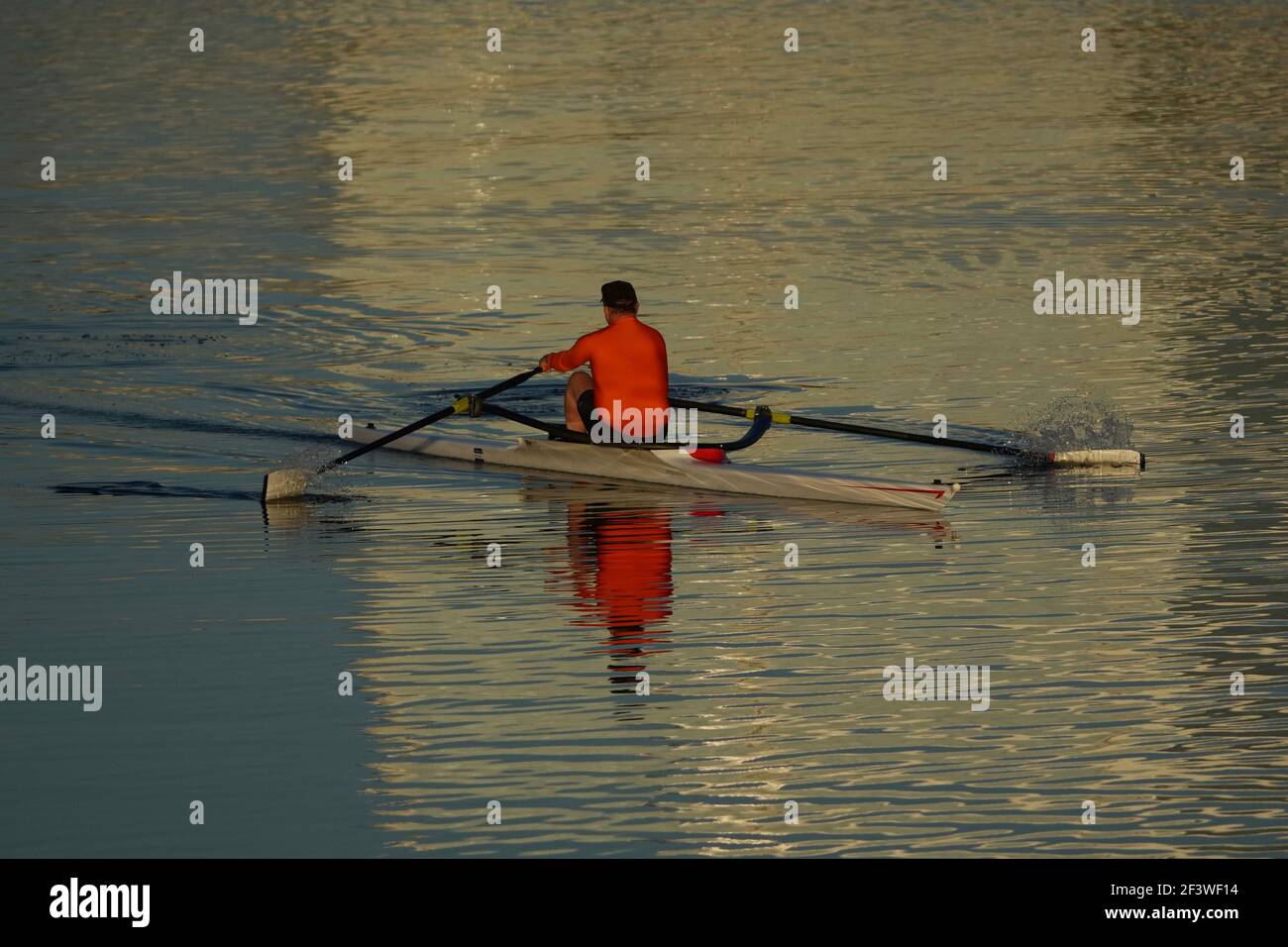 Un uomo non identificabile che indossa una camicia arancione brillante ottiene l'esercitazione kayak in un lago nella mattina presto. Foto Stock