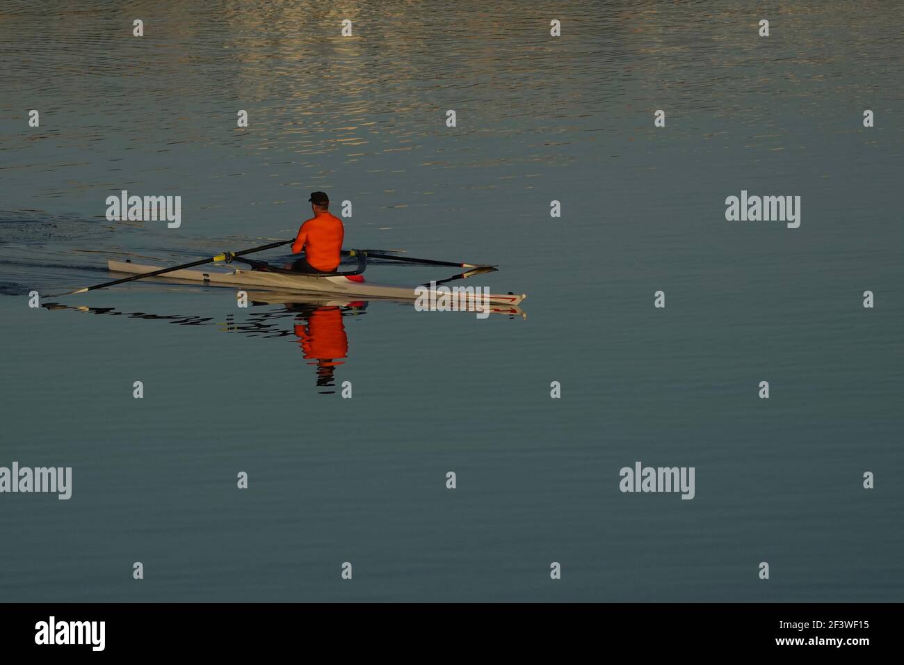 Un uomo non identificabile che indossa una camicia arancione brillante ottiene l'esercitazione kayak in un lago nella mattina presto. Foto Stock