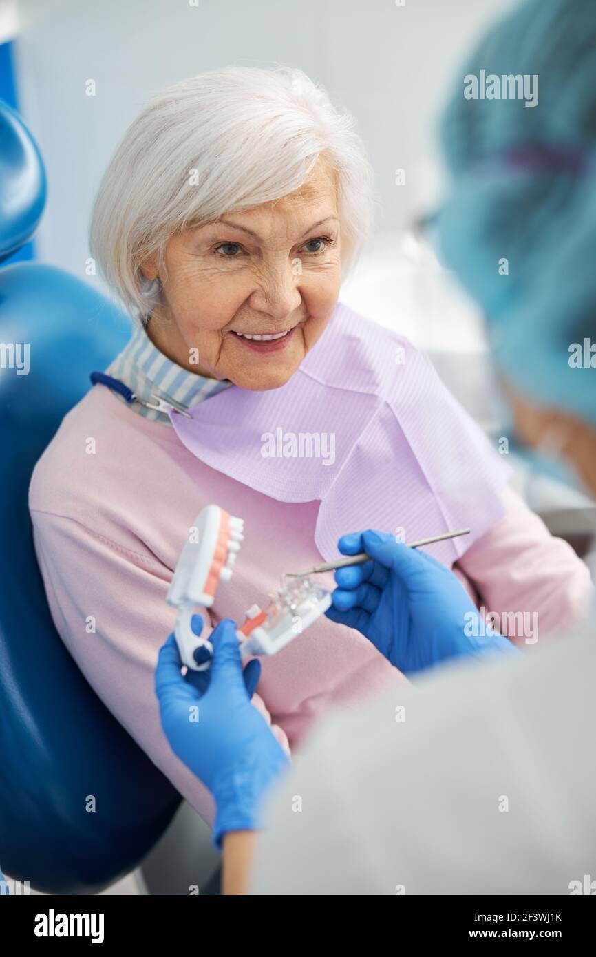 Pensionato interessato che guarda il dentista con modello dentale Foto Stock