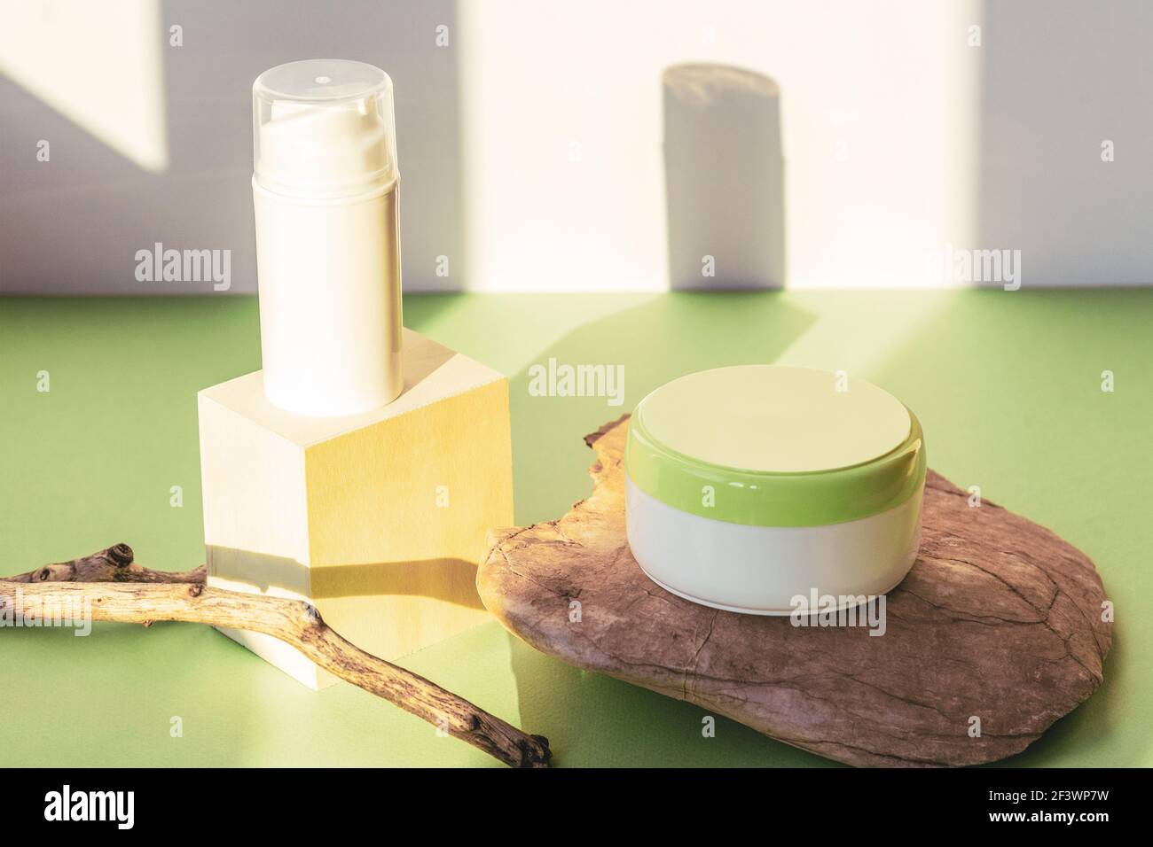 Branding cosmetico e concetto di imballaggio. Cura della pelle siero e crema vaso su pietra naturale su tavola verde in luce solare. Foto Stock