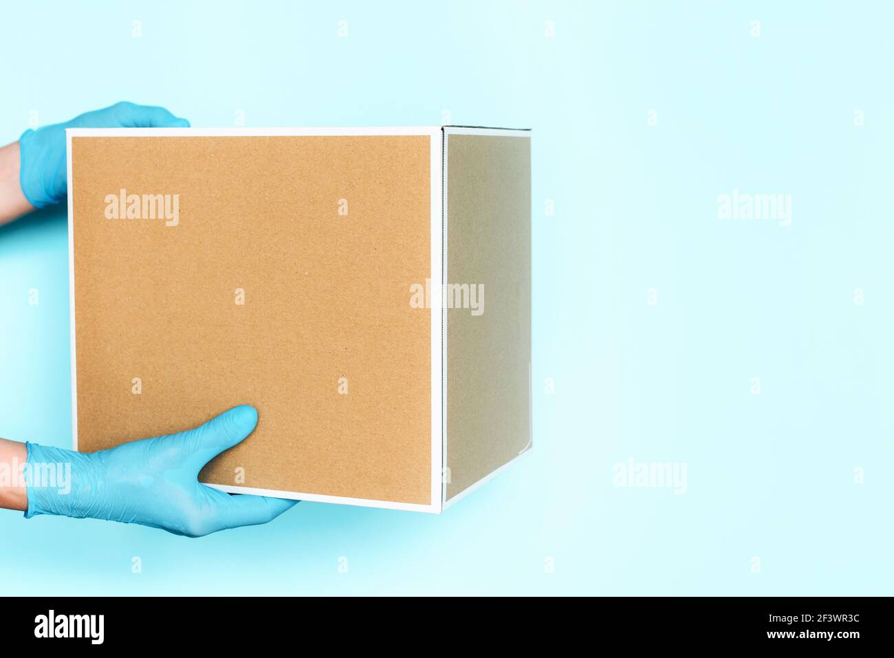 Mano in guanto medico dà scatola di mestiere su sfondo blu. Concetto di shopping online senza contatto. Banner, spazio per la copia. Trasporto di consegna veloce e gratuito Foto Stock