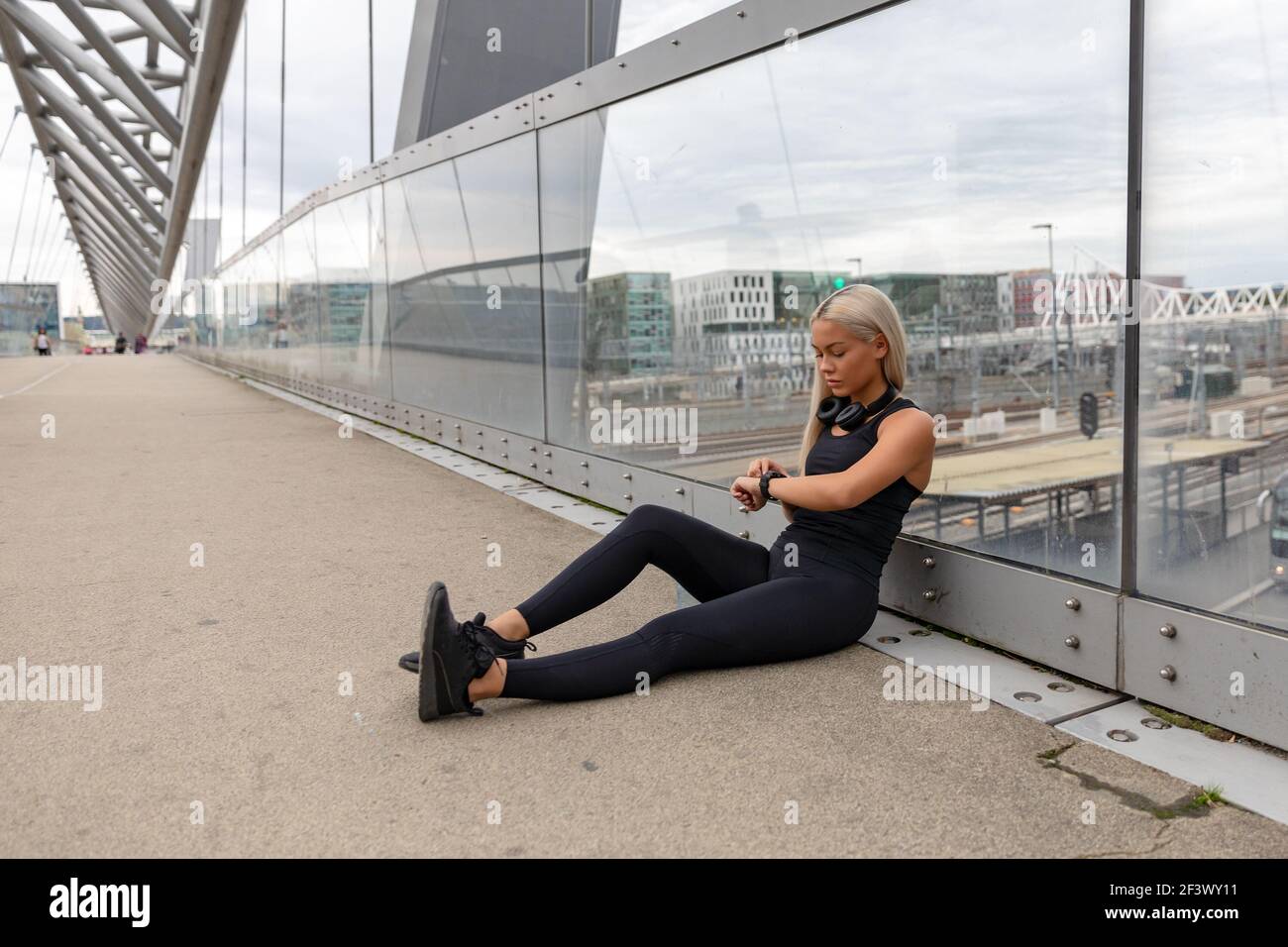 Runner concentrato seduto su Bridge dopo la corsa e controllare l'allenamento Prestazioni Foto Stock