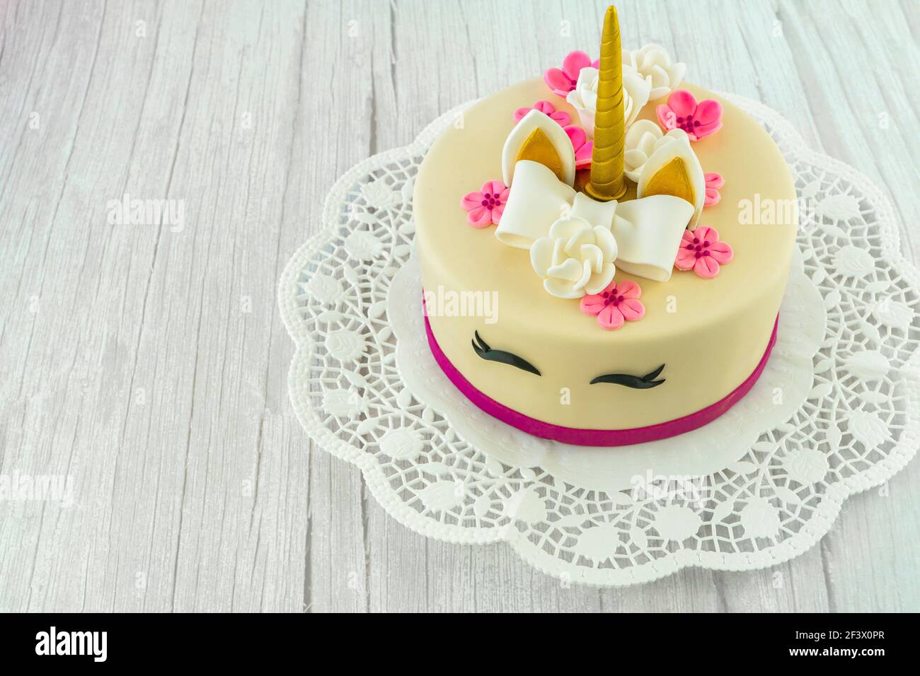 Torta unicorno su sfondo di legno e pizzo. Carino unicorno a strati torta  fatta in casa decorata con prua, fiori di rosa, mais dorato e orecchie.  Spazio di copia Foto stock -