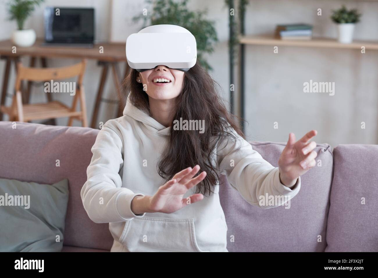 Donna a casa indossando cuffie per la realtà virtuale per giocare il divano Foto Stock