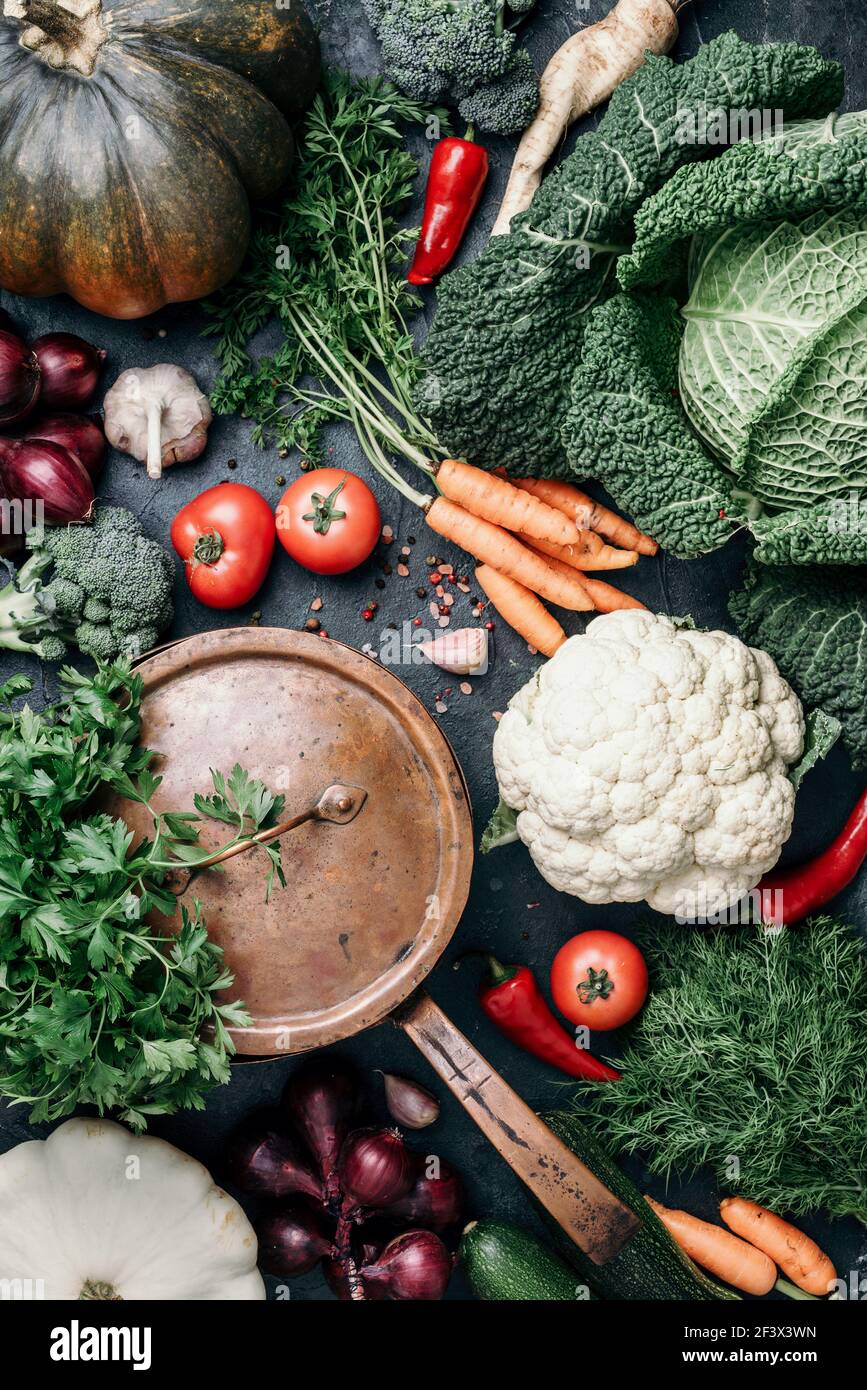 Pentola di rame, erbe, cipolla viola, zucca, pomodoro, broccoli, pepe, cavolo, carota, prezzemolo, calafiore, zucchine su sfondo scuro. Vista dall'alto. Copia Foto Stock