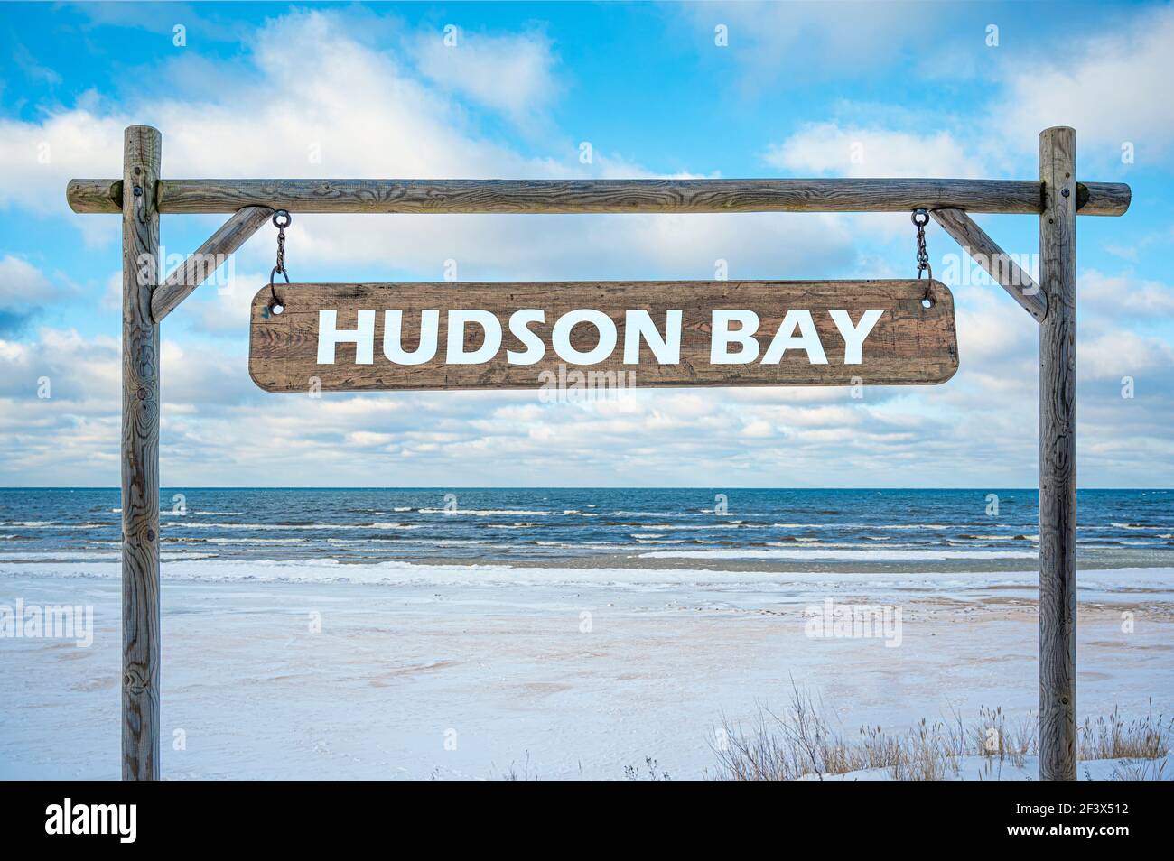 Cartello in legno con baia di Hudson contro mare, cielo blu e spiaggia con neve bianca. Foto Stock