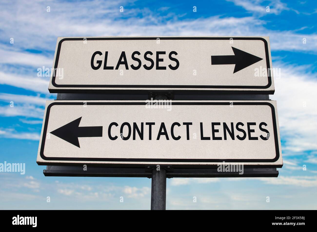 Occhiali contro lenti a contatto segnale stradale con due frecce su sfondo blu cielo. Due cartelli stradali bianchi con frecce su palo metallico. Cartello stradale a due vie WIT Foto Stock