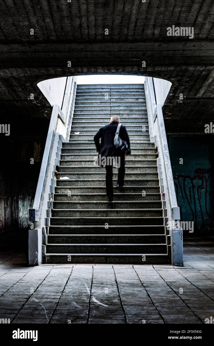 Uomo vestito in nero con borsa a tracolla corre su scale lontano dal passaggio sporco Foto Stock
