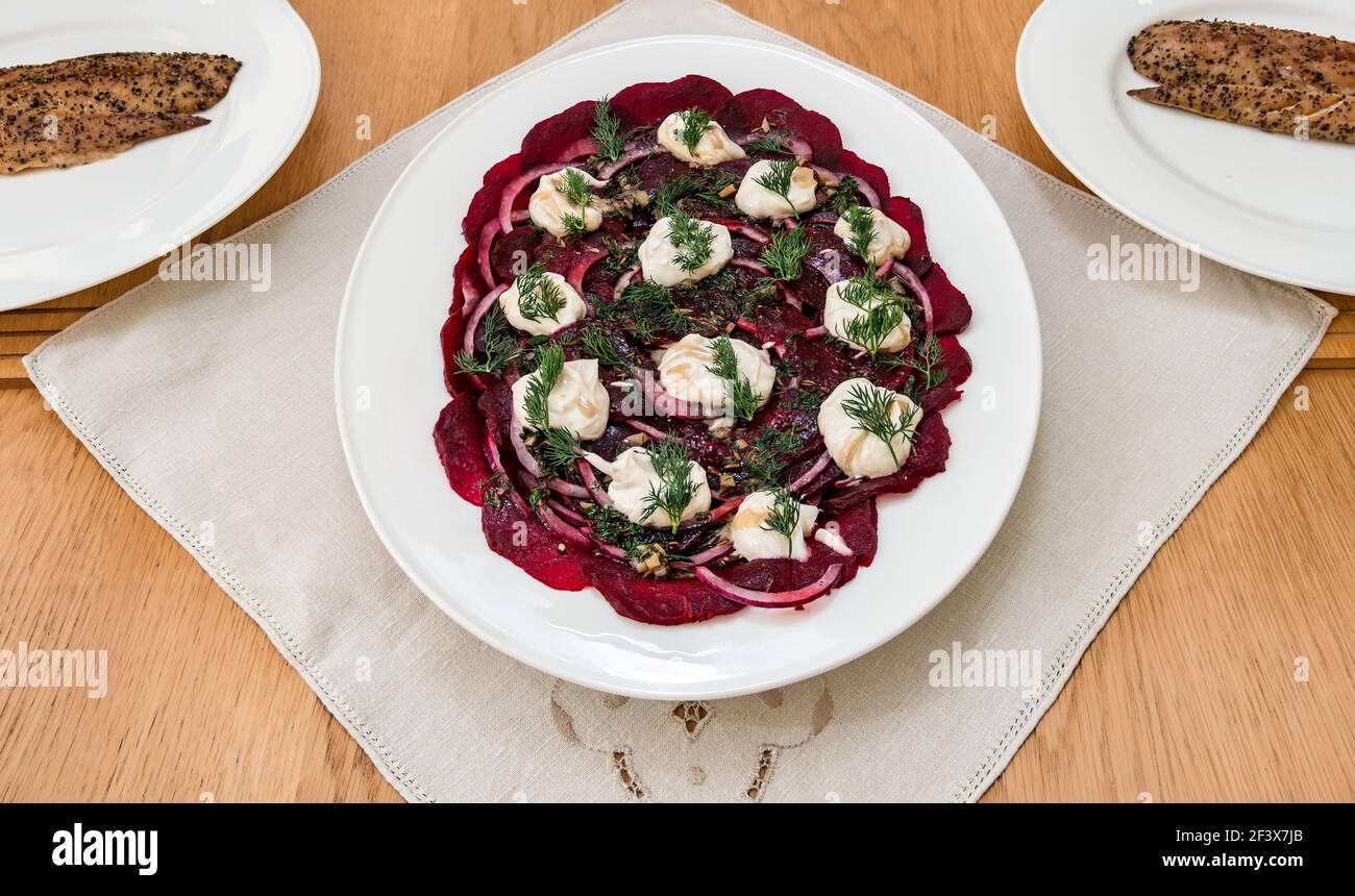 Insalata di barbabietole servita su piatto bianco con cipolle rosse, dilll e yogurt con sgombro affumicato al peperone sui piatti della cena Foto Stock