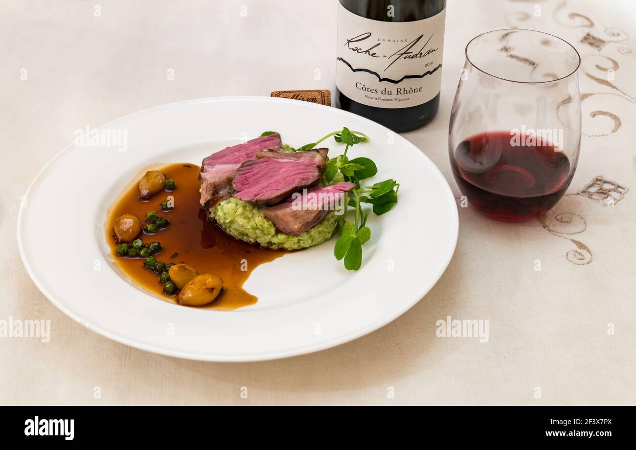 Agnello con risotto, piselli e cipolle caramellate, bicchiere di vino e bottiglia di vino rosso Cote du Rhone Roche Audran Foto Stock