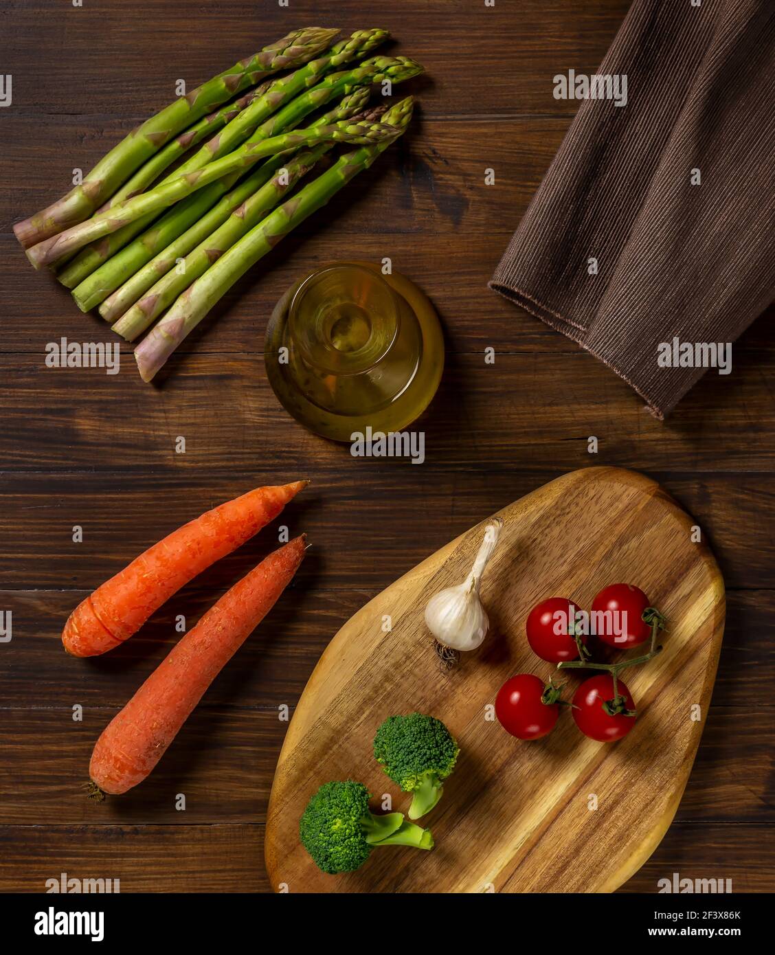 Composizione di verdure varie con asparagi, pomodori ciliegini, carote, aglio, broccoli e crostate con olio d'oliva, su tavola di legno e cutt di legno Foto Stock