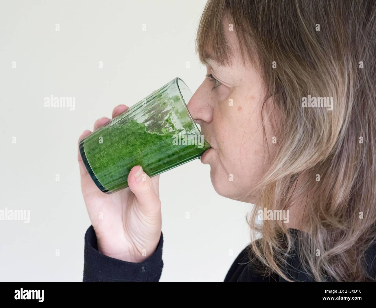 Una donna prende un drink di frullato verde brillante da una vista trasparente vetro.laterale Foto Stock